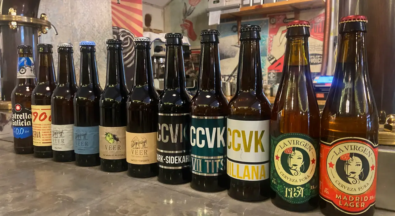Lineup of craft beer bottles including Estrella Galicia, Veer, CCVK and La Virgen Madrid Lager along a bar counter