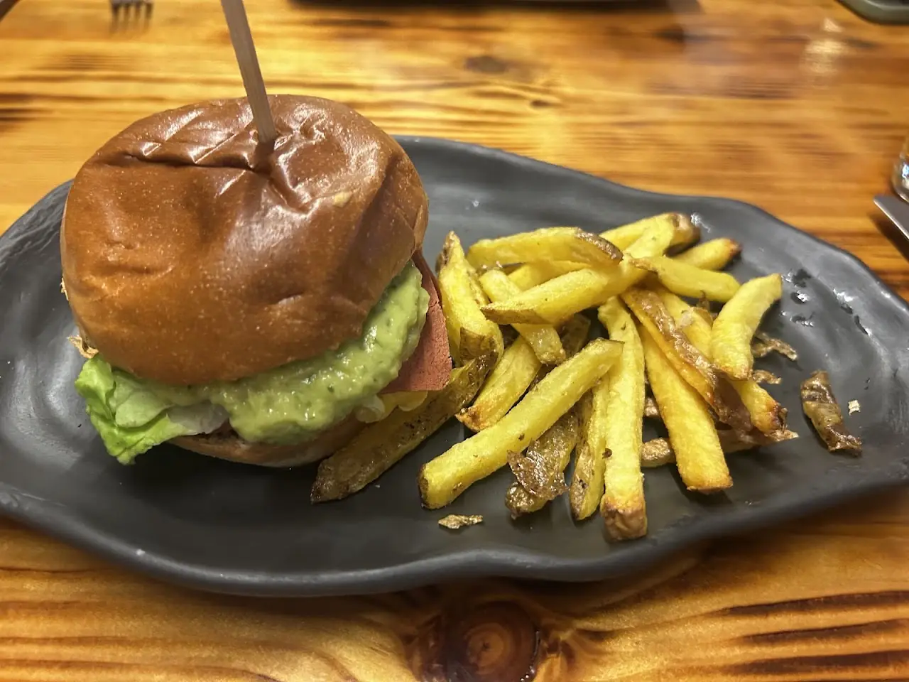 A burger with melted cheese and lettuce on a brioche bun, served with french fries.