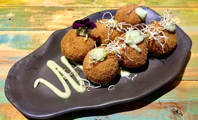 Breaded croquettes arranged on a dark plate with a drizzle of white sauce.