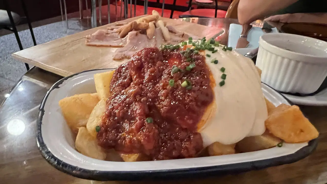 Fried potato wedges topped with red sauce, alioli and chives, jamon board behind