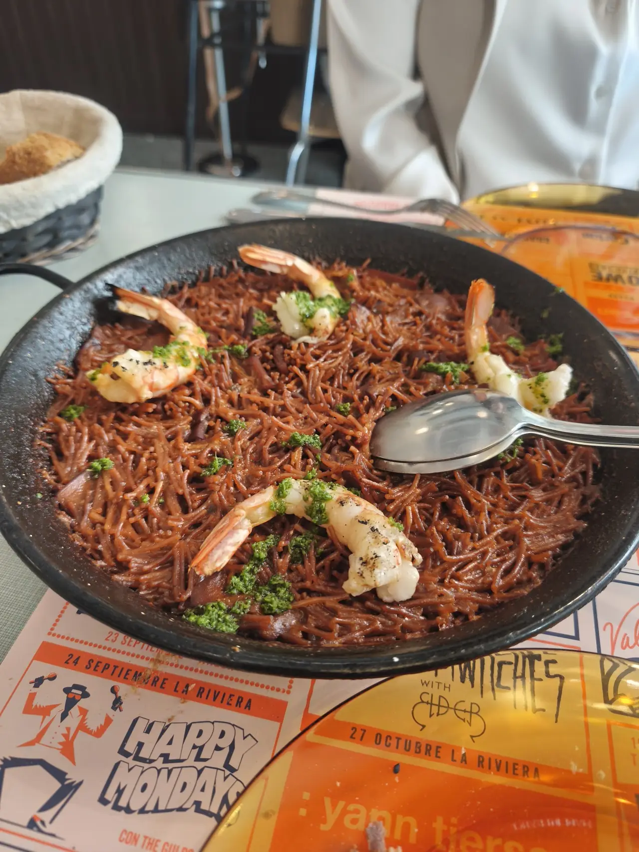 Black fideua noodles with prawns and green herb sauce served in a metal pan