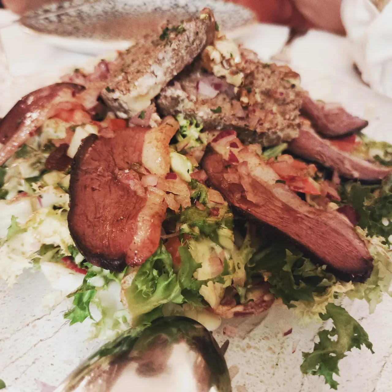 A salad topped with seared duck or meat strips and herbs