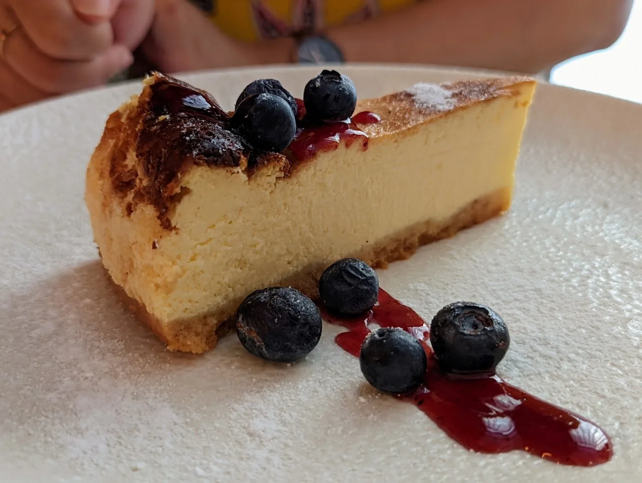 A slice of cheesecake topped with blueberries and berry sauce