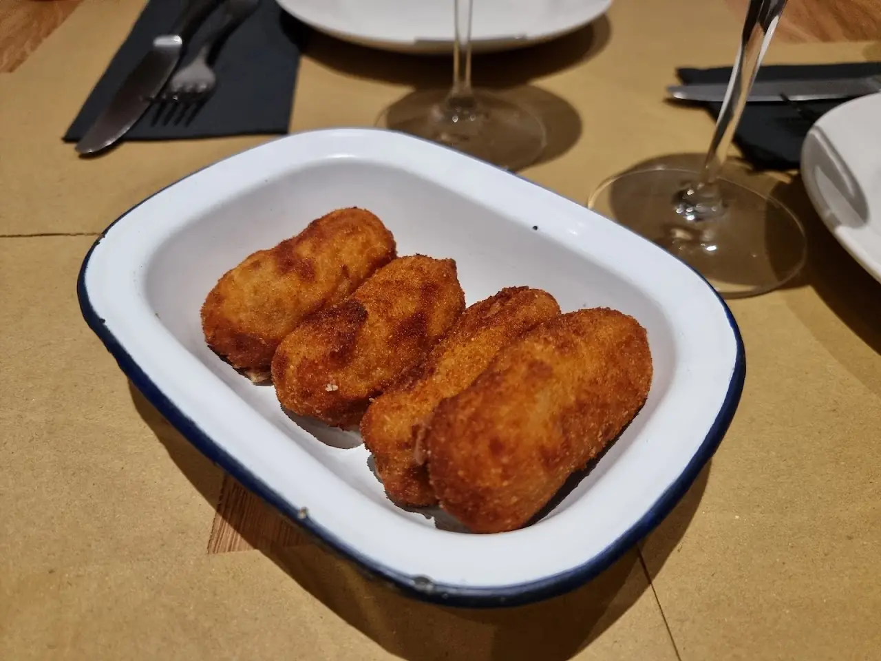 Four breaded croquettes in a white enamel dish.