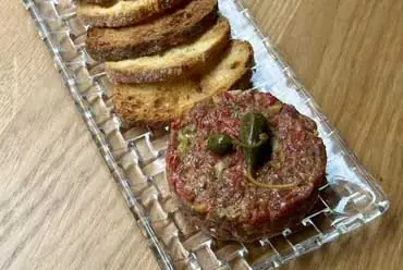 Steak tartare topped with capers, served alongside slices of toasted bread