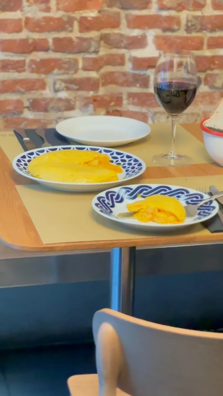 Two blue and white plates of soft yellow potato omelette on a wooden table next to a glass of red wine