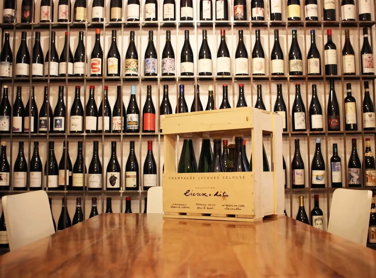 A wall of wine bottles behind a wooden table with a wooden wine box on it