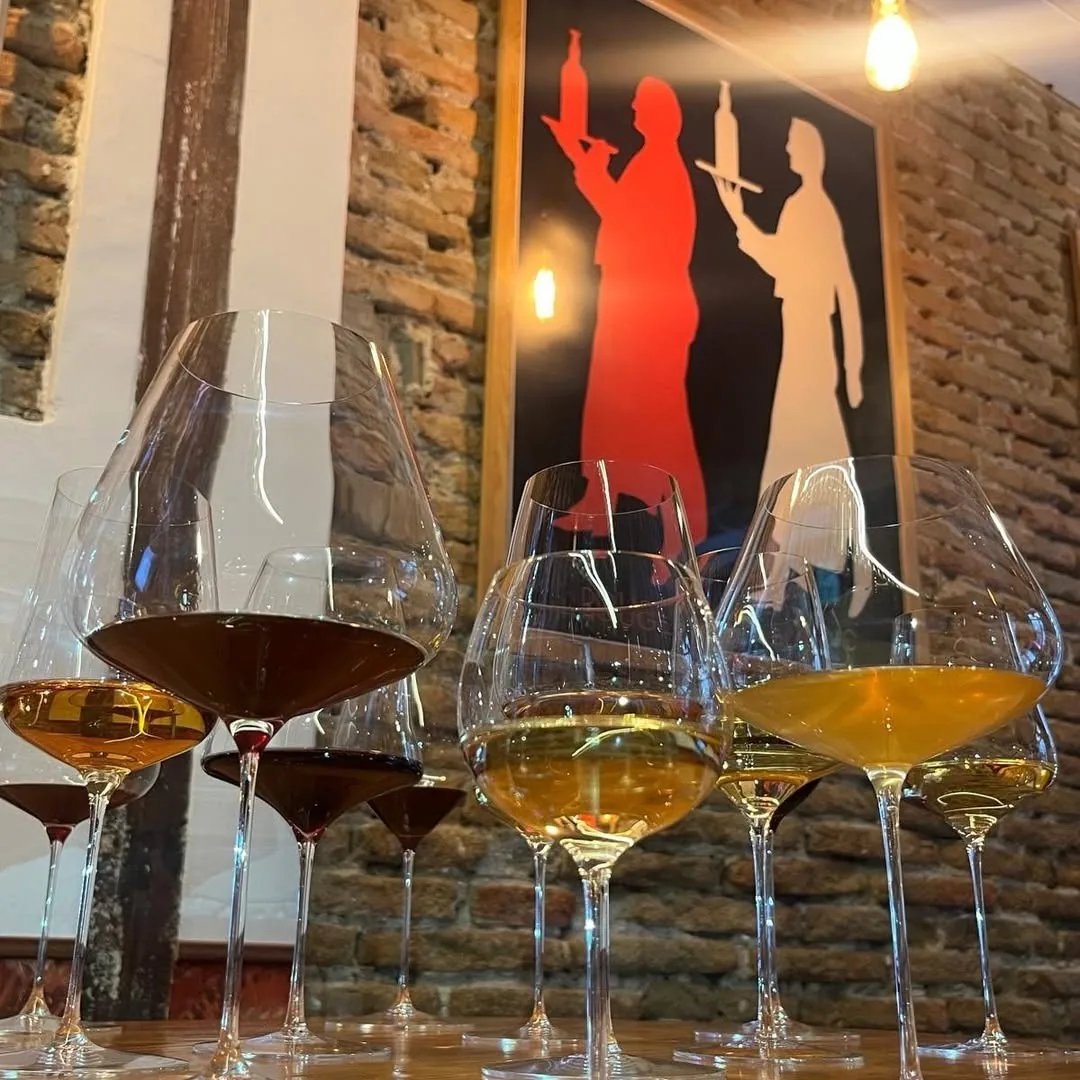 Several wine glasses holding orange and white wine in front of a brick wall