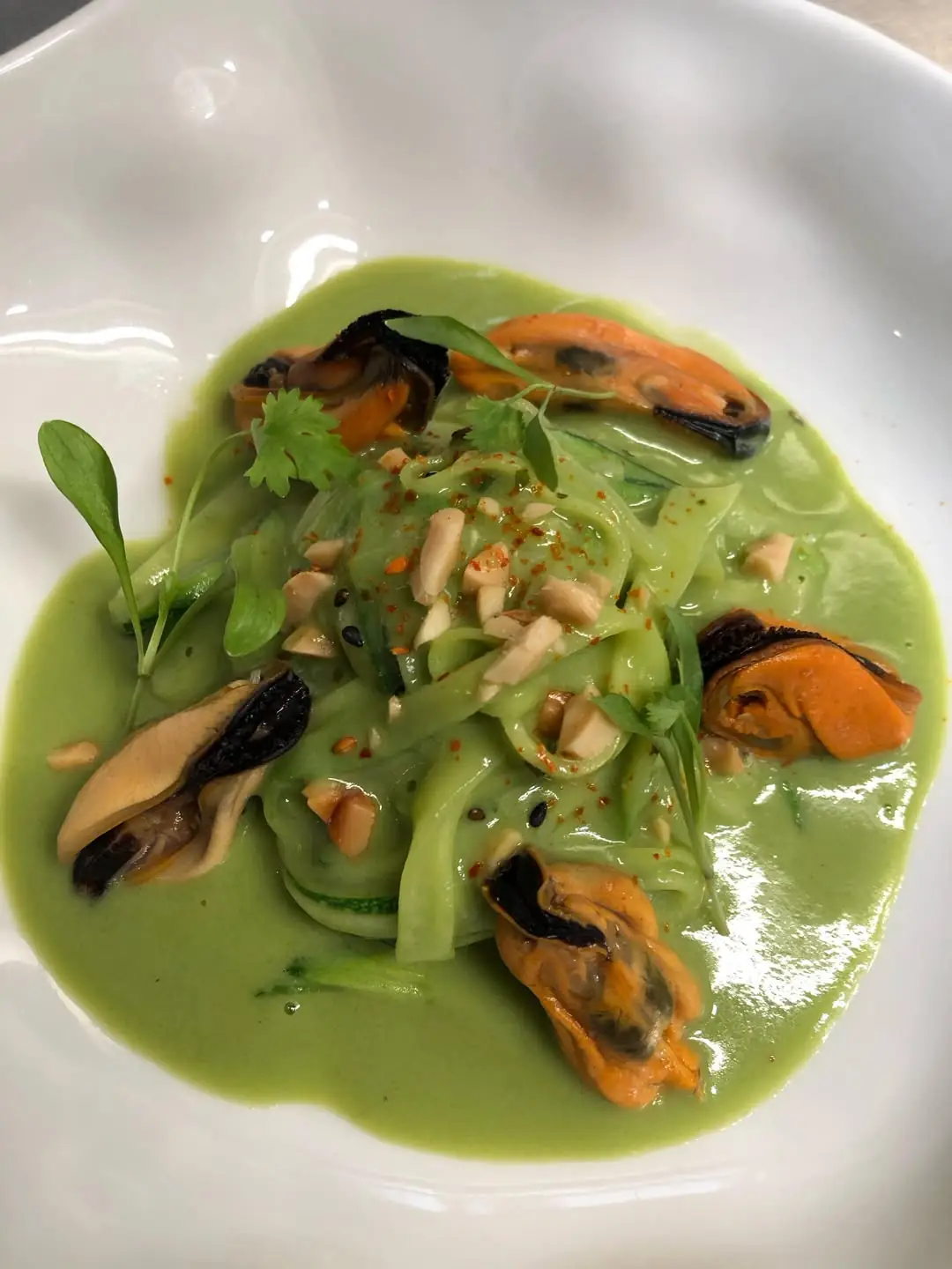 Seafood pasta dish with open mussels in a bright green herb sauce