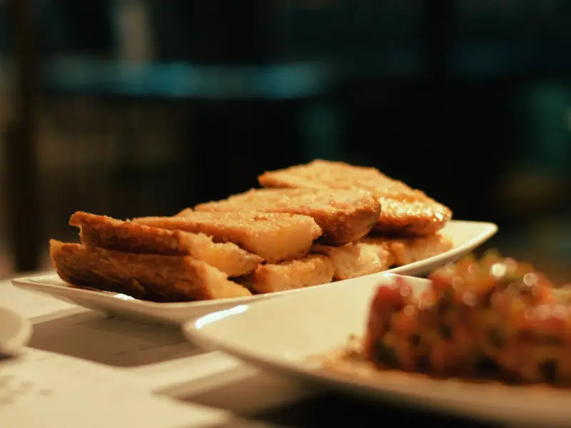 Crispy fried pork belly slices on a white plate, with a tomato tartare in the foreground, at La Flauta