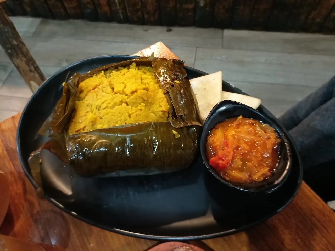 A tamale wrapped in banana leaf with a side of tomato salsa