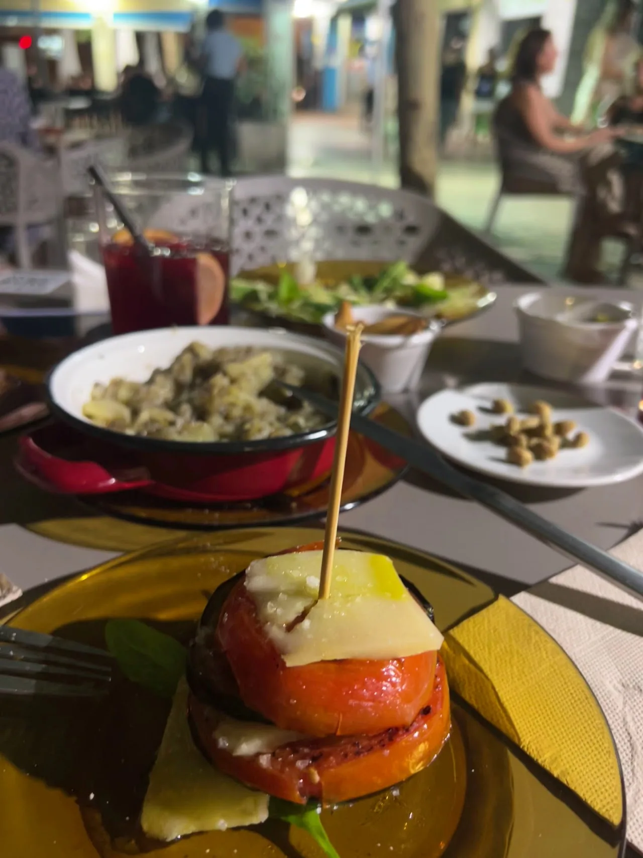A skewer of melted cheese and tomato beside small tapas plates