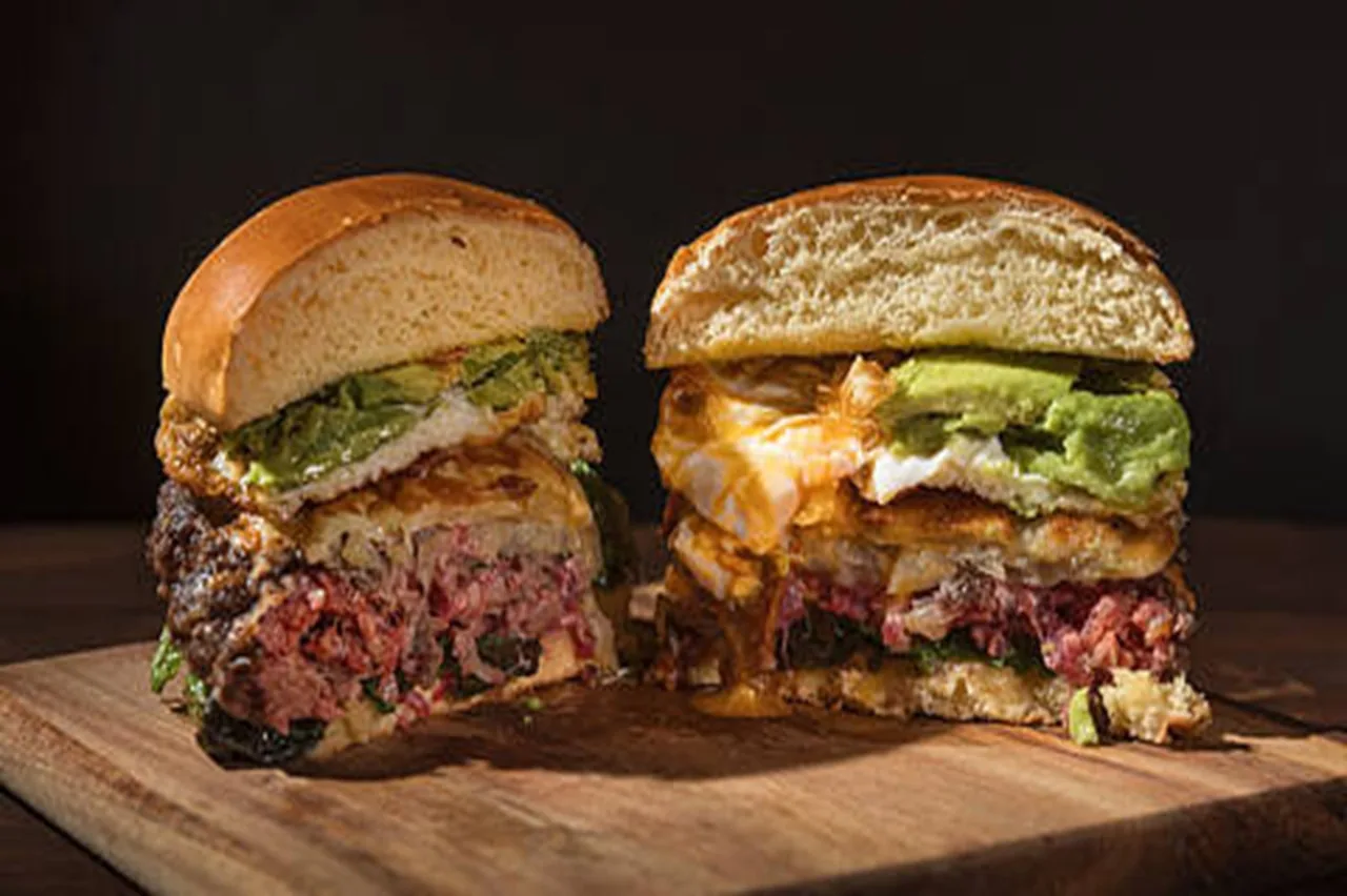 A burger cut in half on a wooden board showing a thick patty, egg and toppings