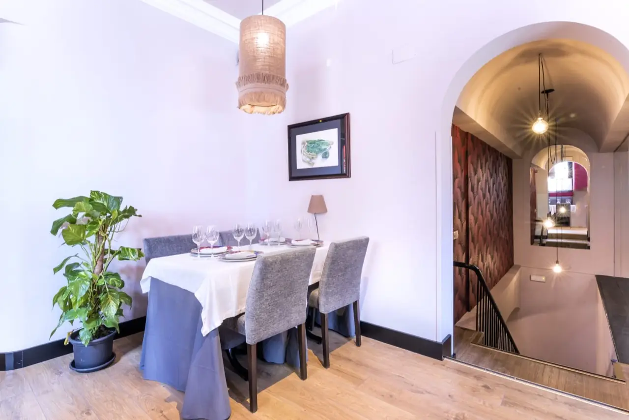 Private dining nook with a table set for four beside a potted plant and an arched doorway leading to a staircase and mirror