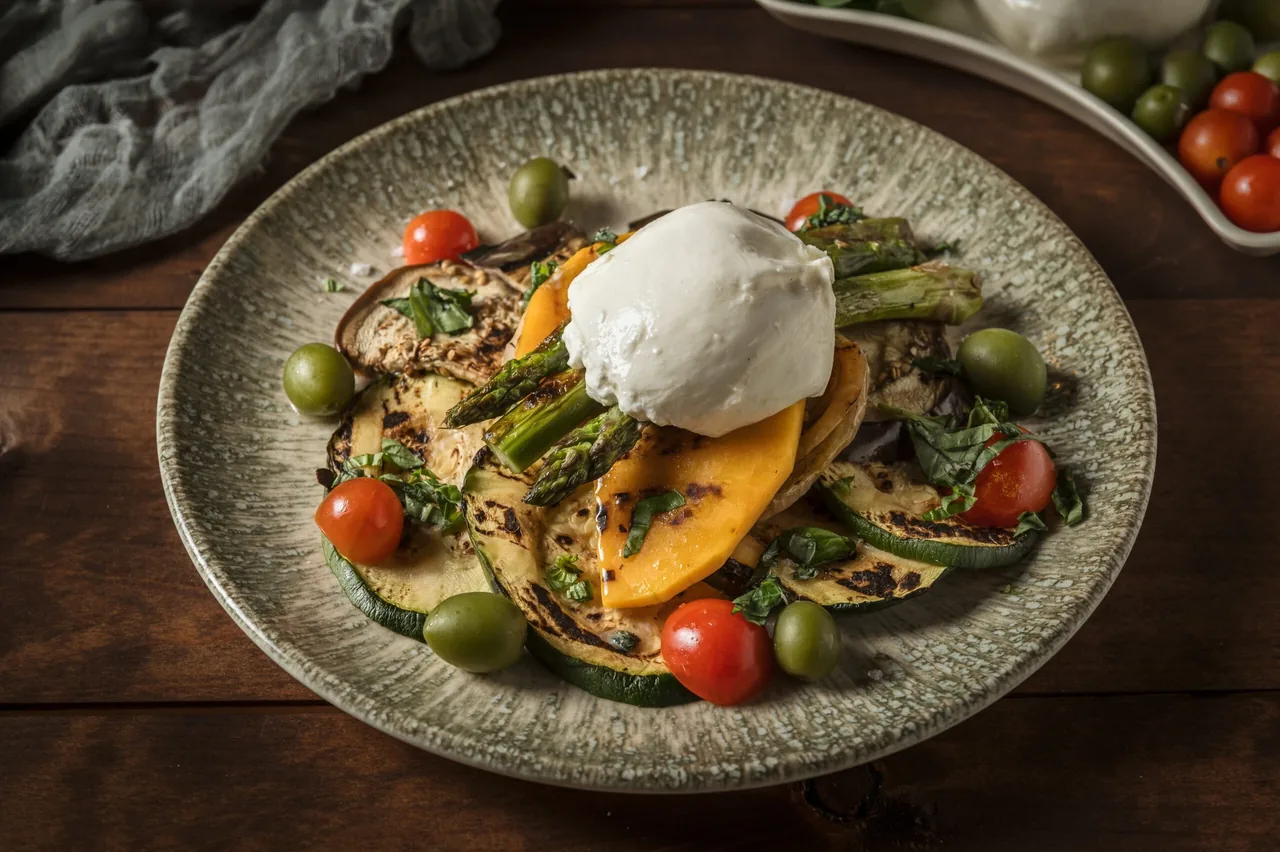 A round plate of salad with a scoop of white cheese, sliced vegetables and cherry tomatoes