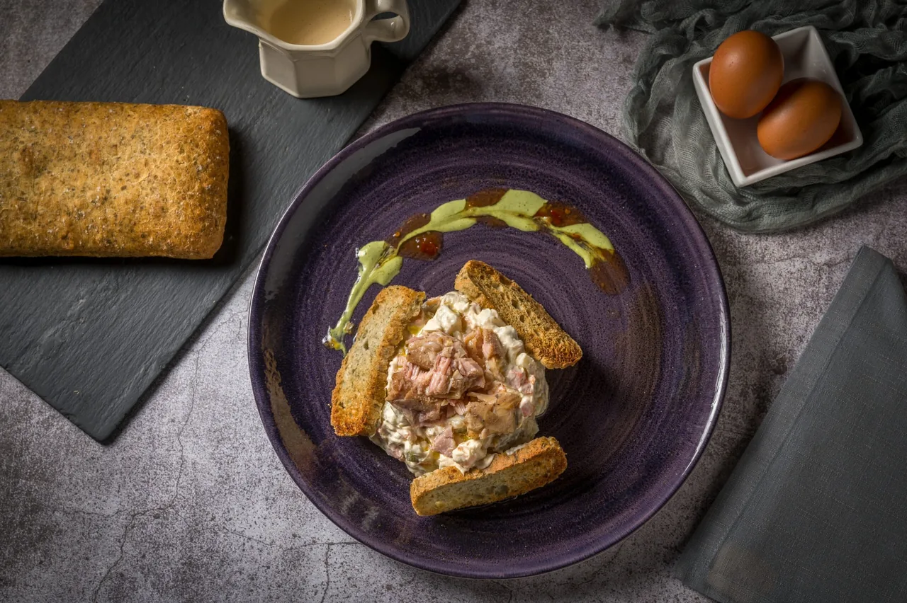 A dark plate of shredded meat and a golden fried block on a grey stone surface