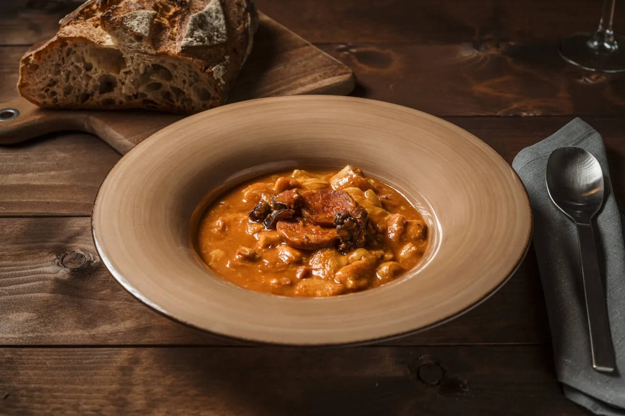 A wide brown bowl of stew with bread on a wooden table