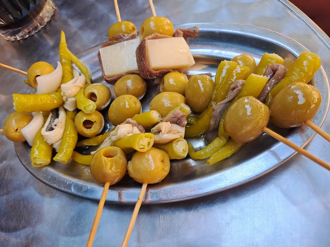 Assorted gilda skewers with olives, pickled peppers, anchovy and cheese on a metal plate