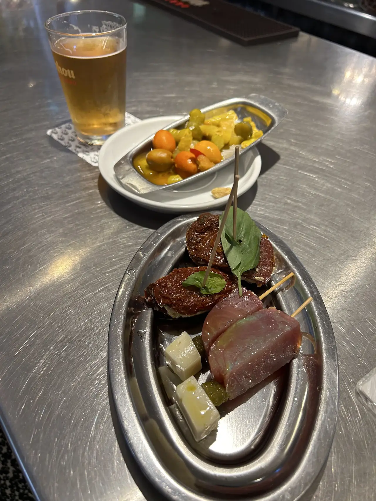 Beer and plates of pinchos including tuna skewers, cheese and olives on the bar