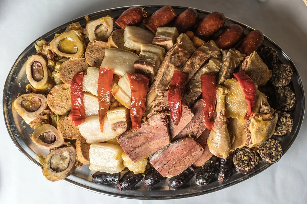A large oval platter piled with boiled meats, sausages and red peppers