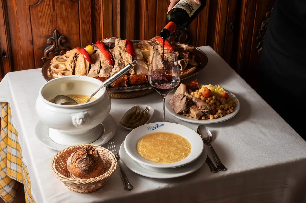 A table set with a platter of meats, a tureen and bowls of soup in a wood-panelled room