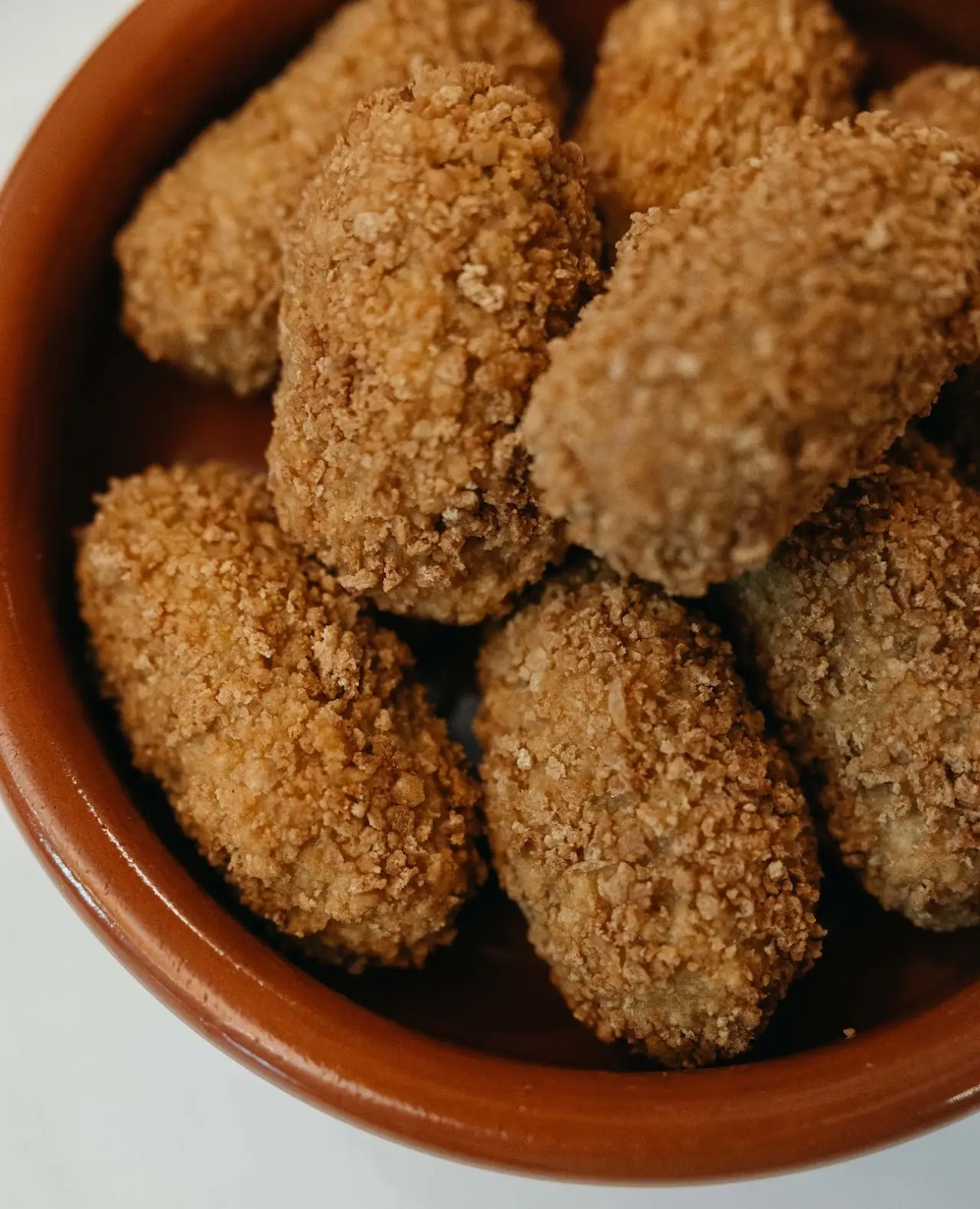 Breaded croquetas piled in a terracotta dish