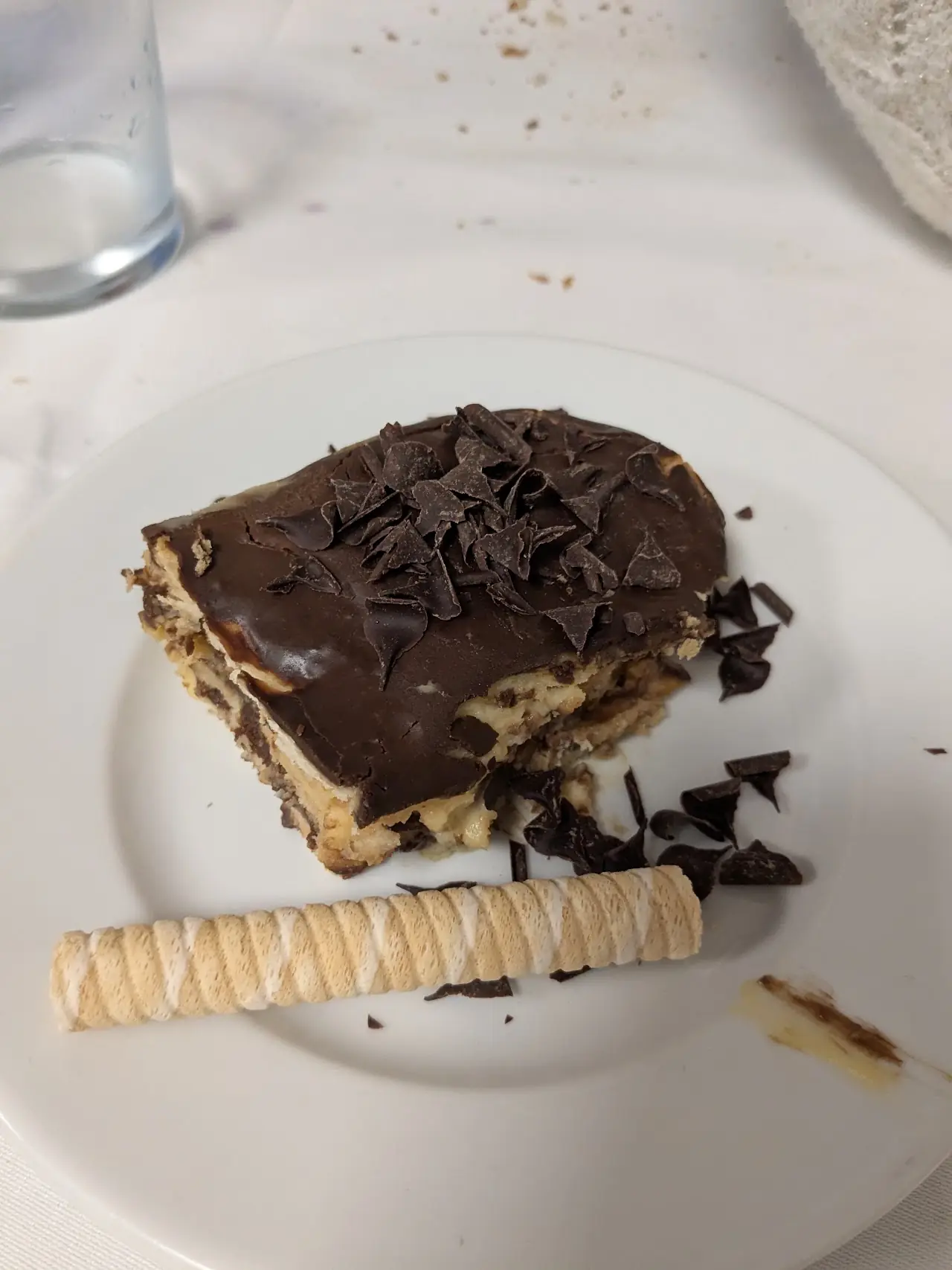 A slice of layered chocolate tiramisu-style cake on a plate with a rolled wafer