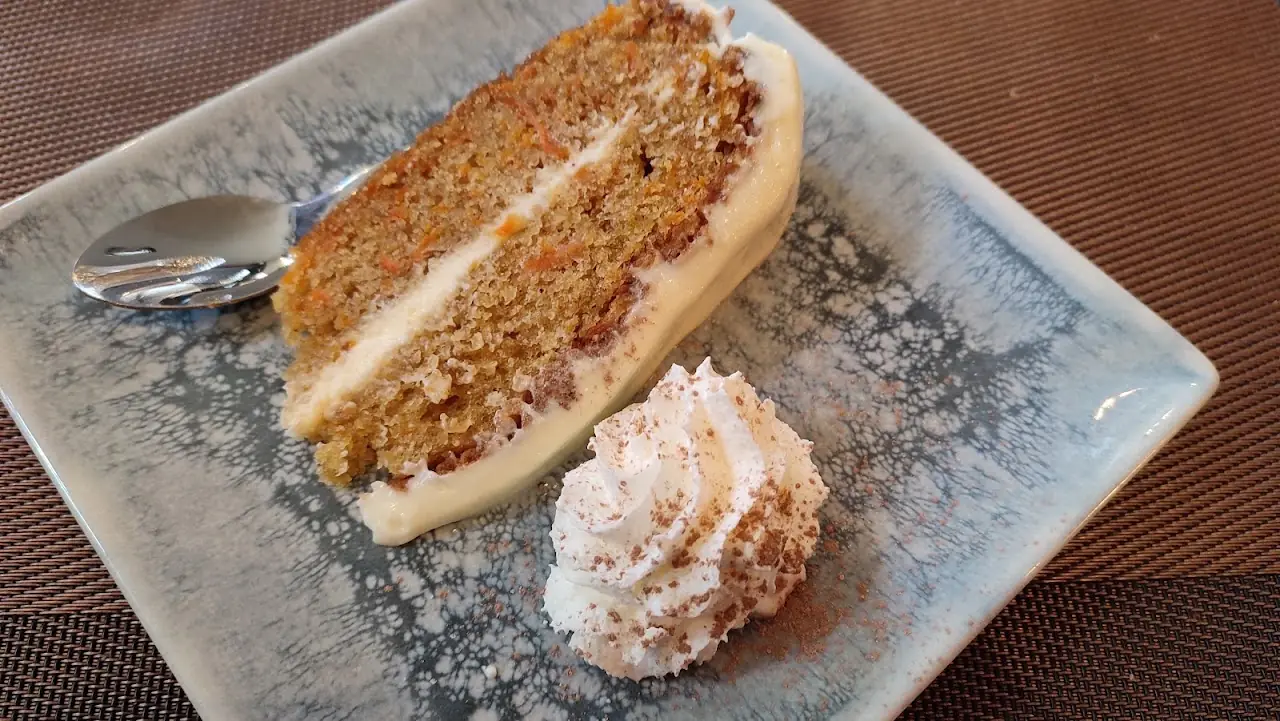 Slice of carrot cake with cream on a grey plate, at La Granota & Co.