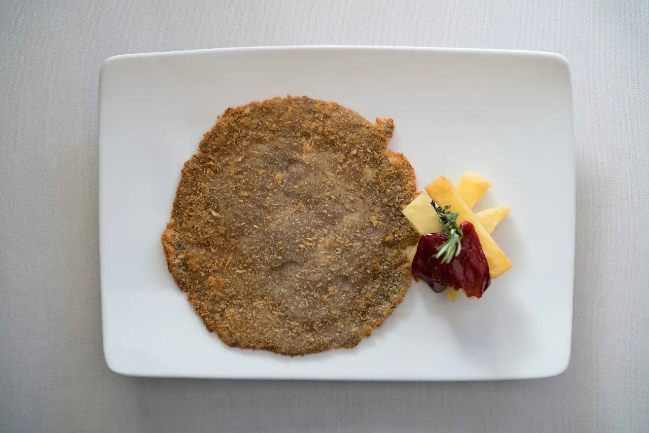 A breaded cutlet on a rectangular plate with a small pile of diced fruit and a dollop of sauce