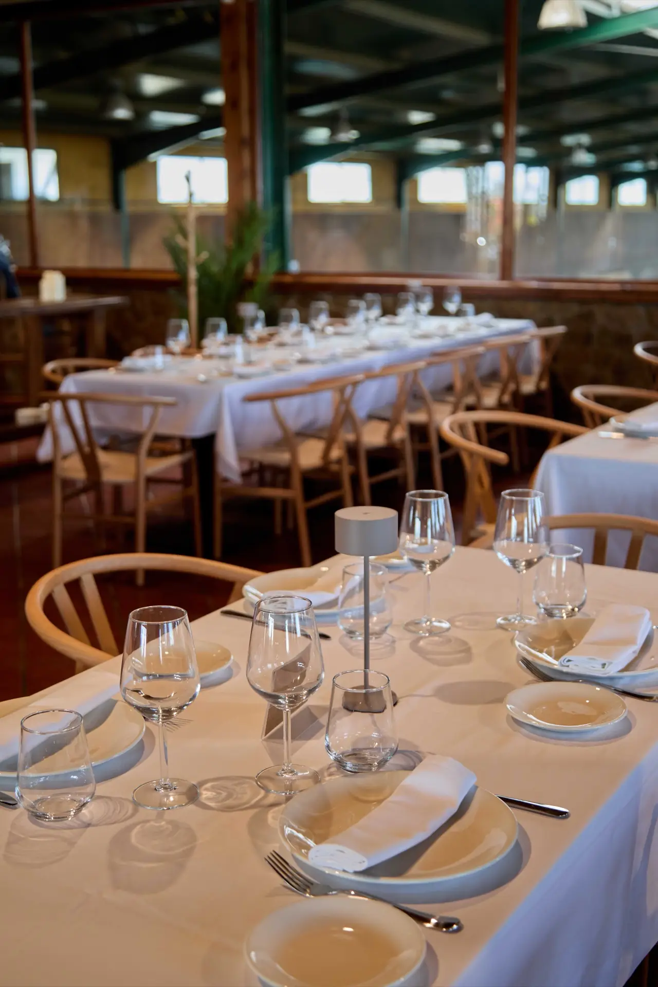 Restaurant dining room with white-linen tables set with wine glasses and wishbone chairs in a glass-walled space