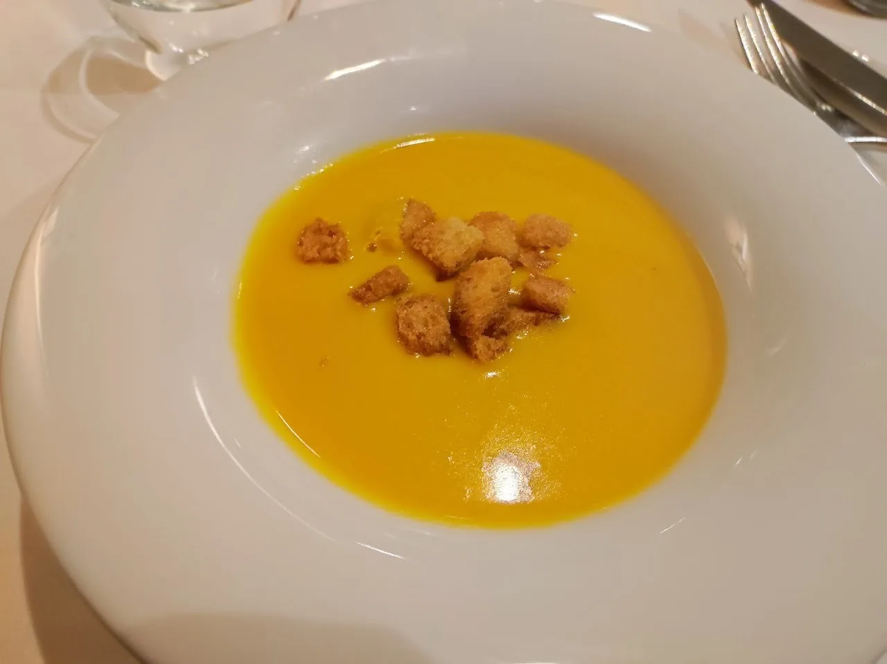 A white plate of smooth orange cream soup topped with small croutons