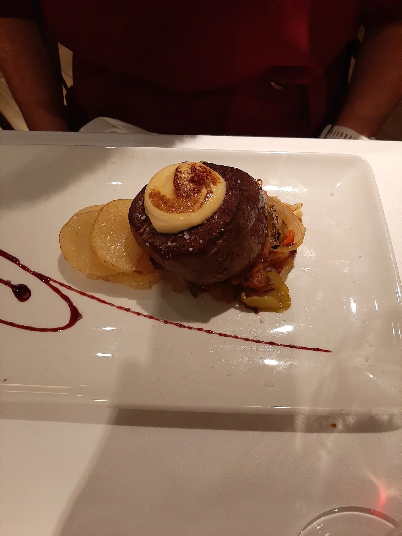A plated meat dish with a glazed roll and sliced potatoes in a red sauce