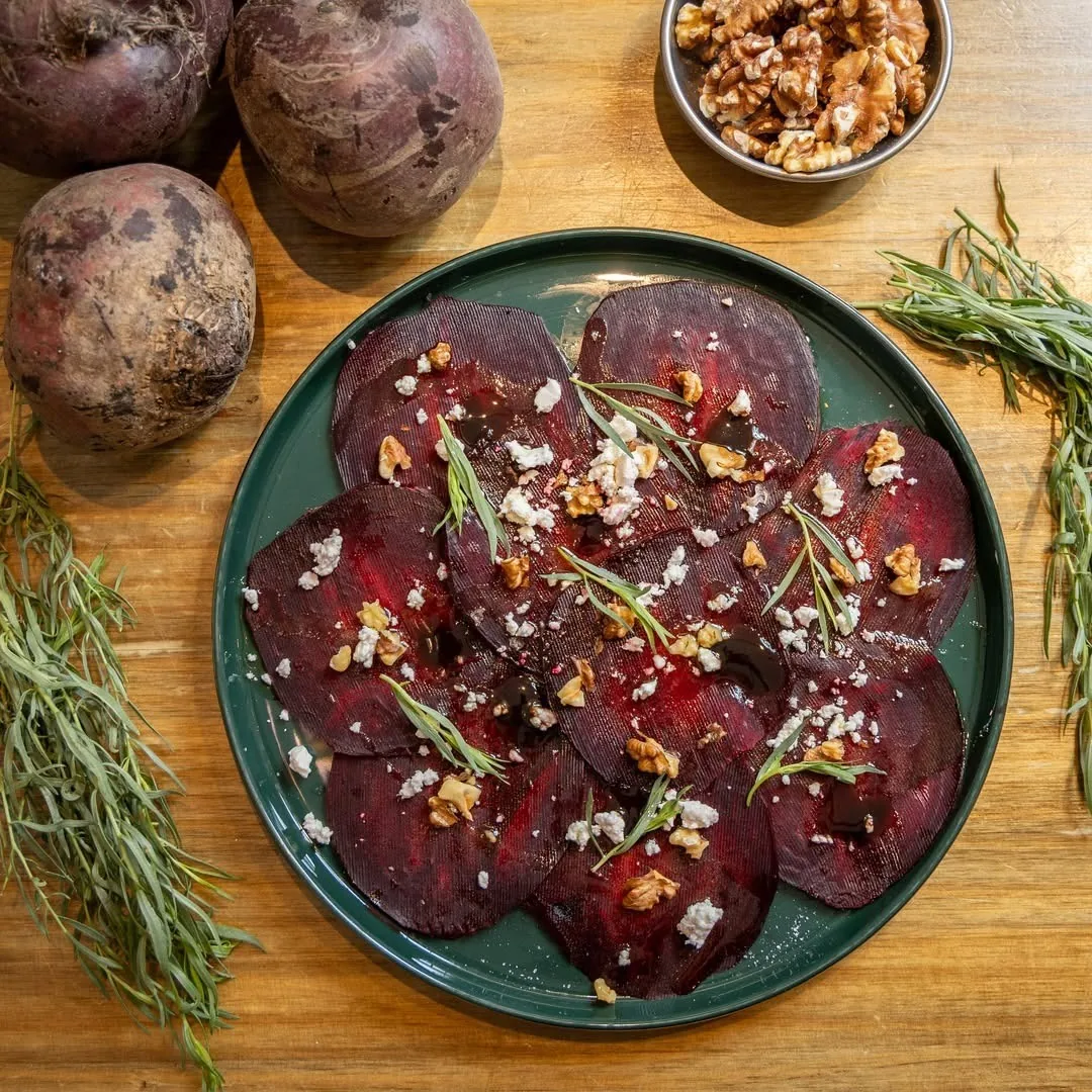 A round plate of sliced beetroot with herbs and nuts