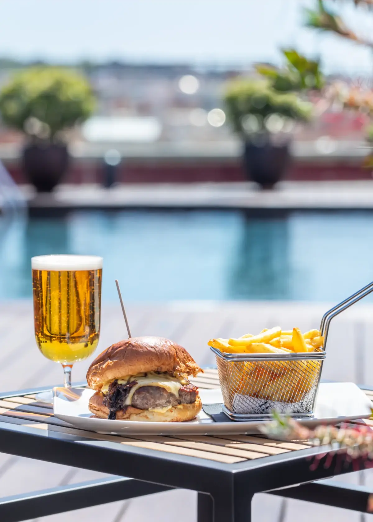 Cheeseburger with caramelized onion and a side of fries in a metal basket, served poolside with a glass of beer, at La Isabela Hotel 1898