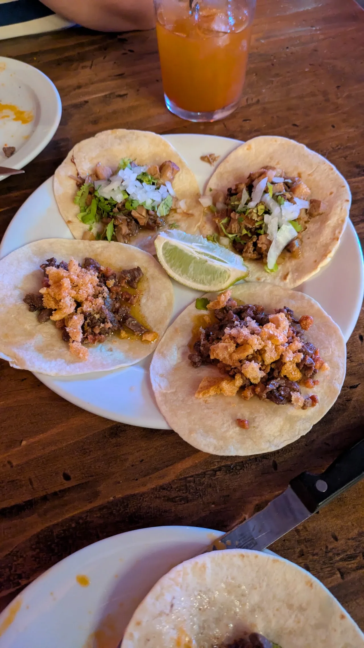 A plate of four tacos with toppings and a lime wedge