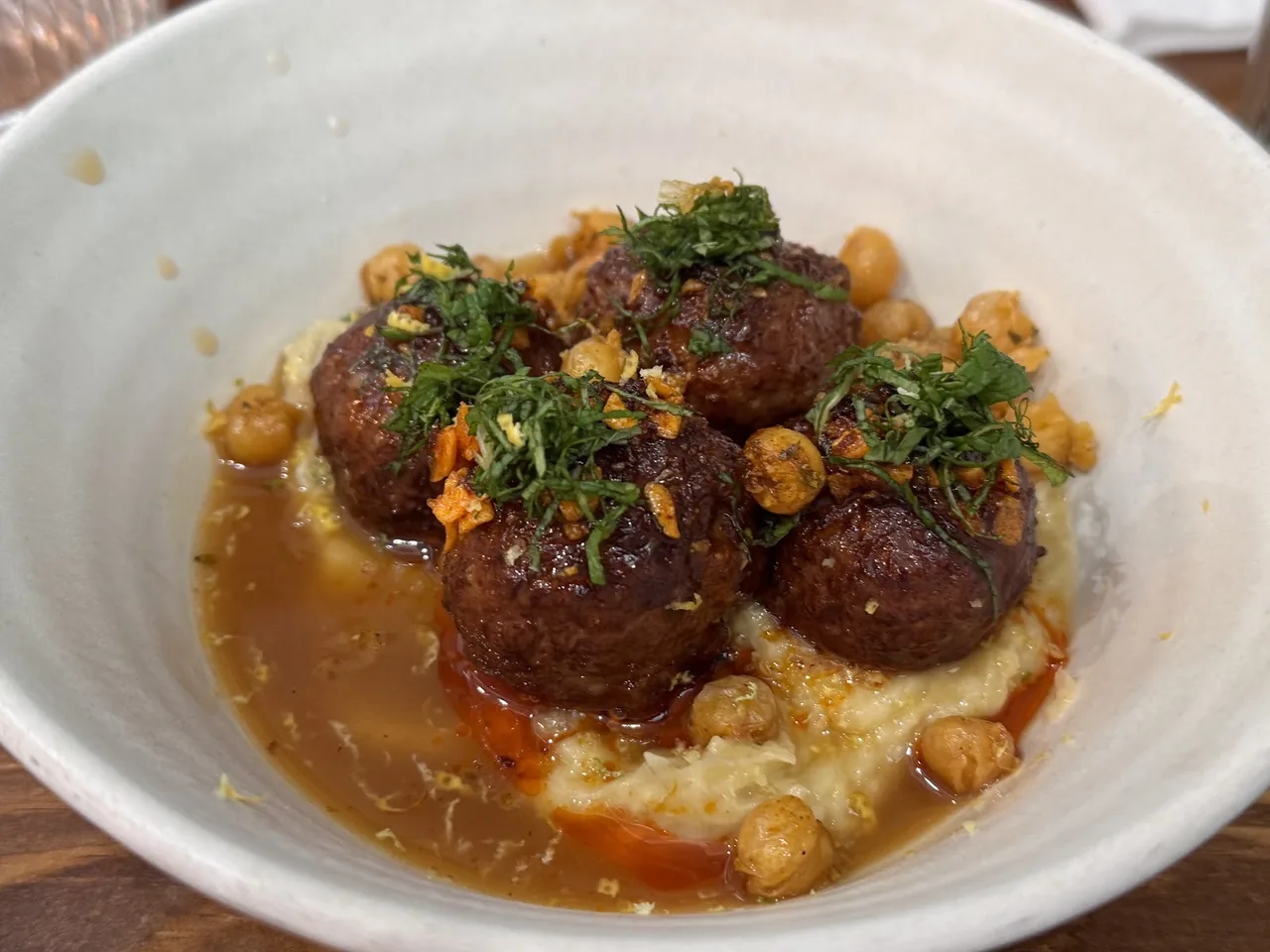 A white bowl of browned meatballs in sauce over a chickpea purée