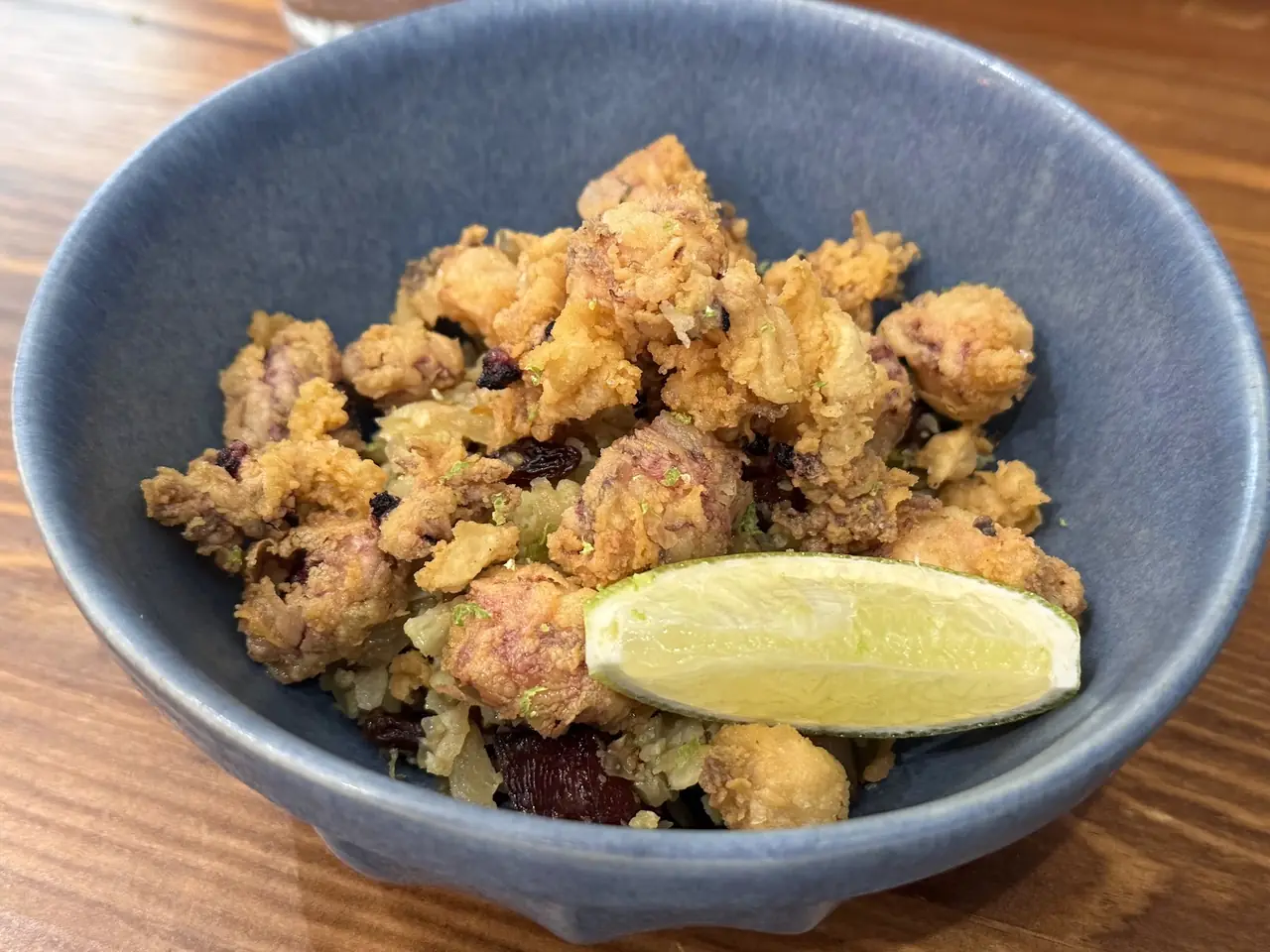 Bowl of fried battered bites with a lime wedge on a wooden table