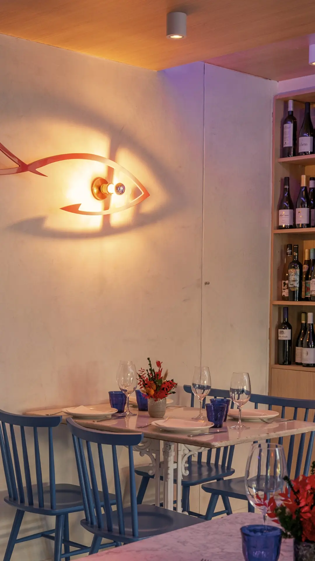 Dining room with a fish-shaped wall lamp, a set table, and a wine shelf