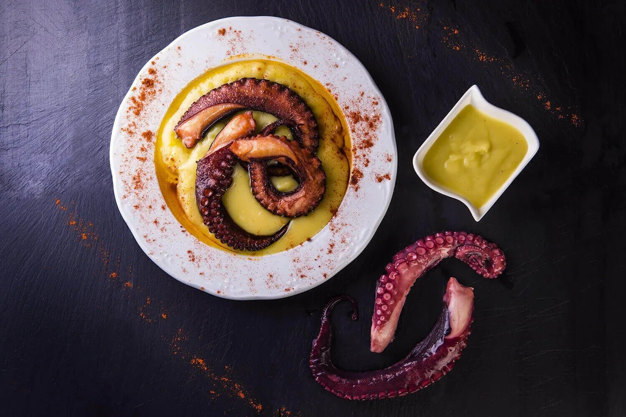 Octopus tentacles on a mashed potato puree with a small dish of sauce