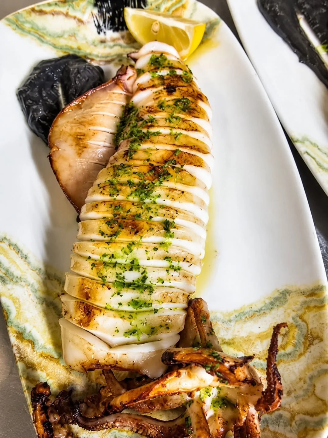A grilled squid on a long plate with herbs