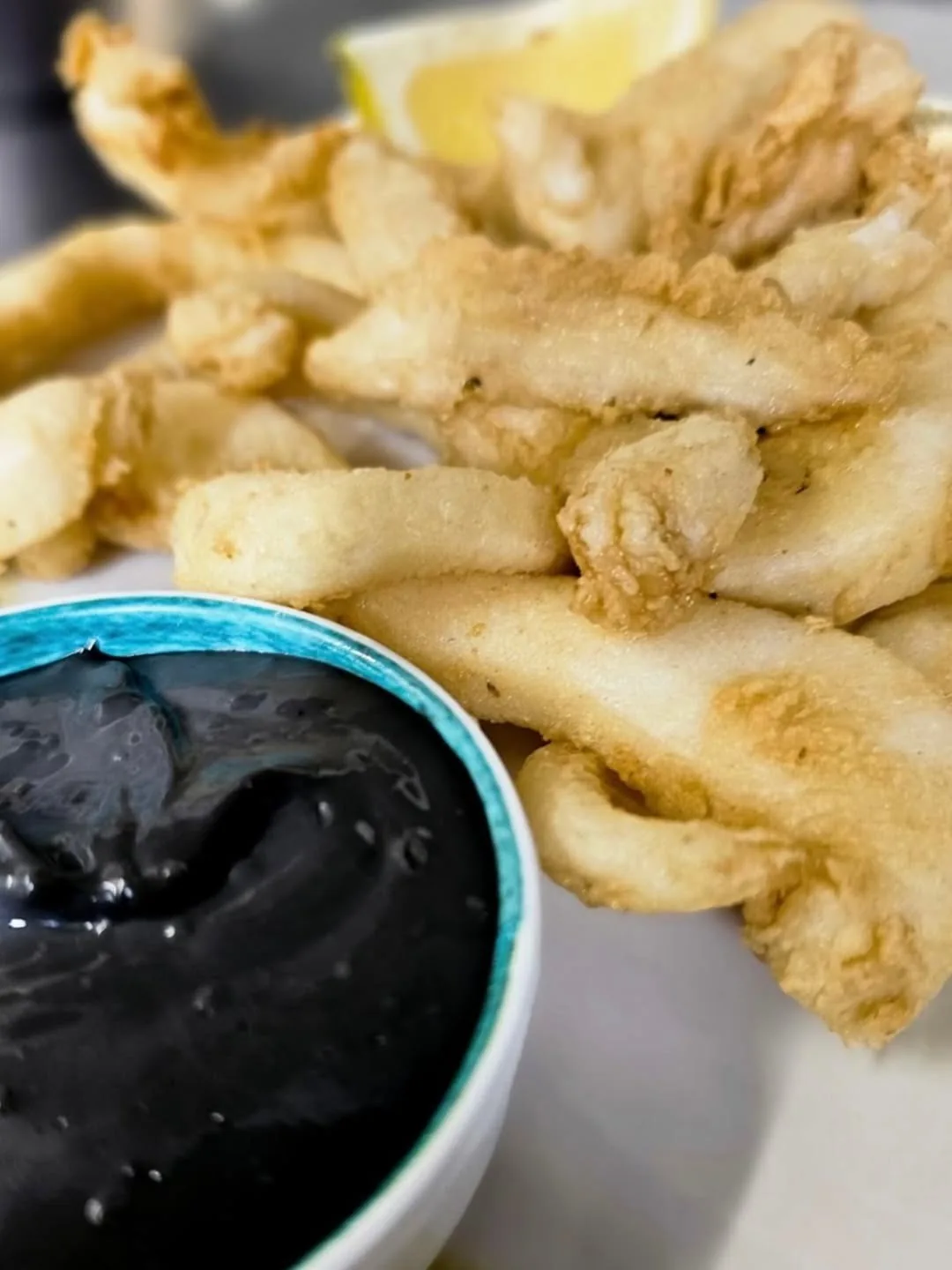 Fried squid rings beside a bowl of black sauce