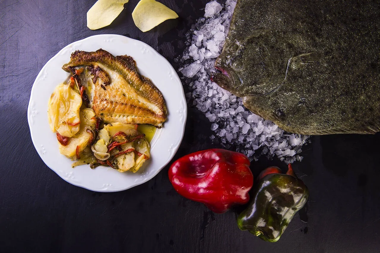 A plate of cooked fish and vegetables beside a sheet of seaweed on coarse salt