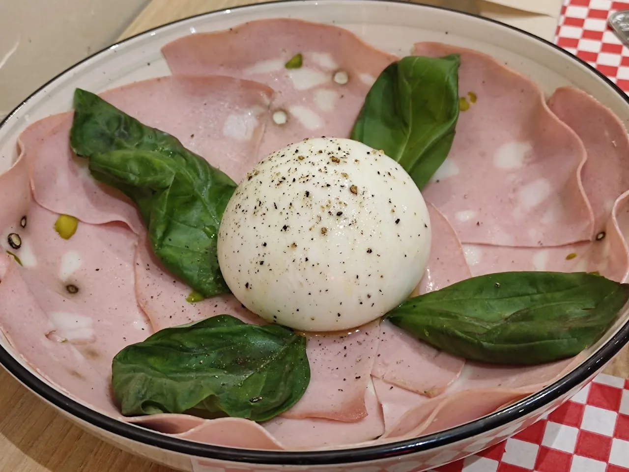 A burrata dish with slices of ham and fresh basil leaves