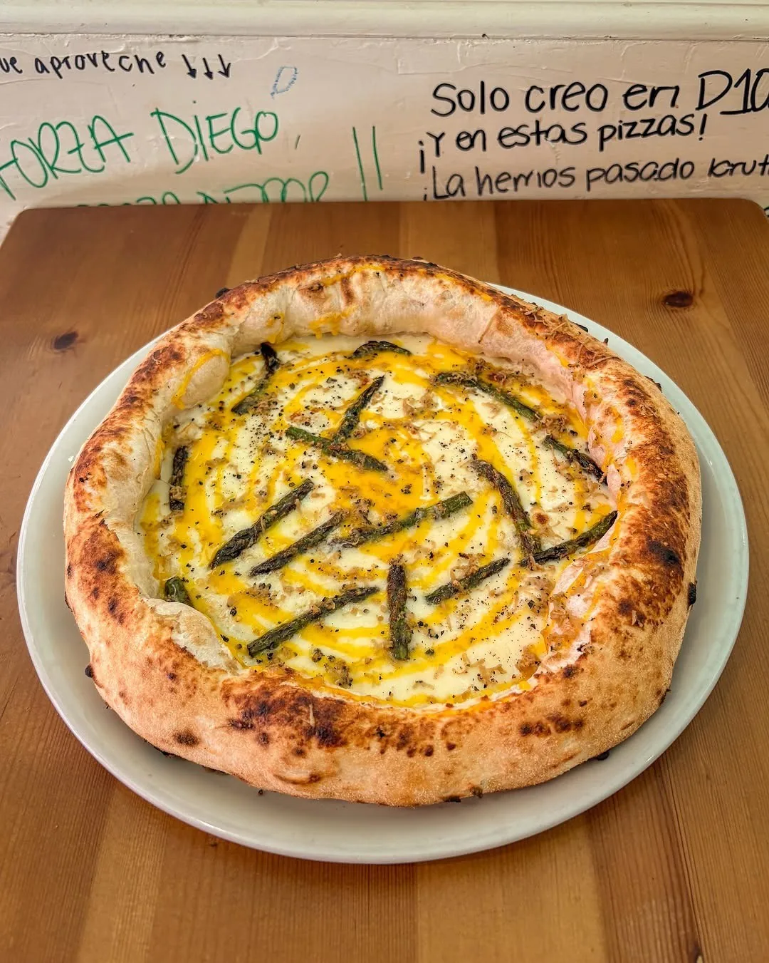 A golden pizza with a yellow cream topping and dark green strips on a white plate