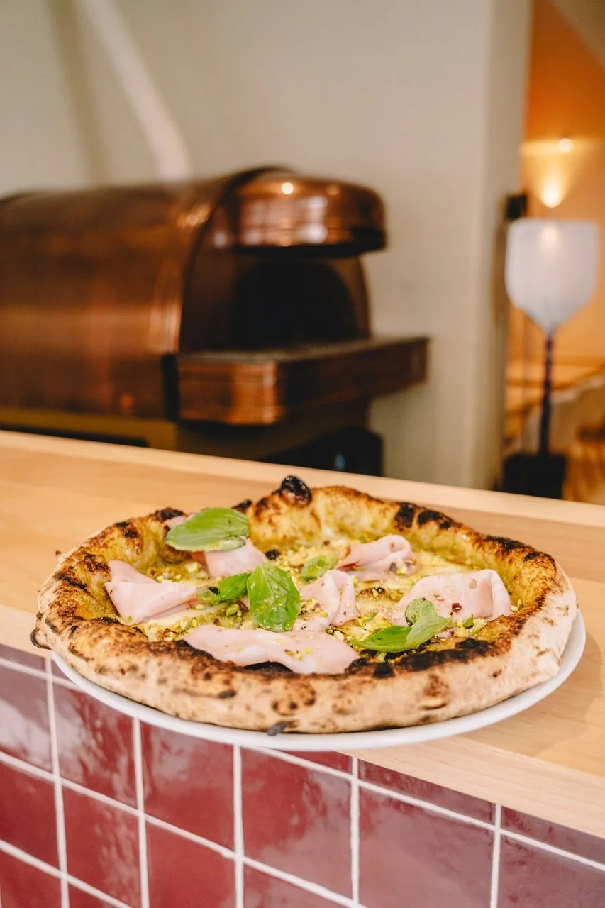 A pizza with a green herb topping resting on a counter with red tiles