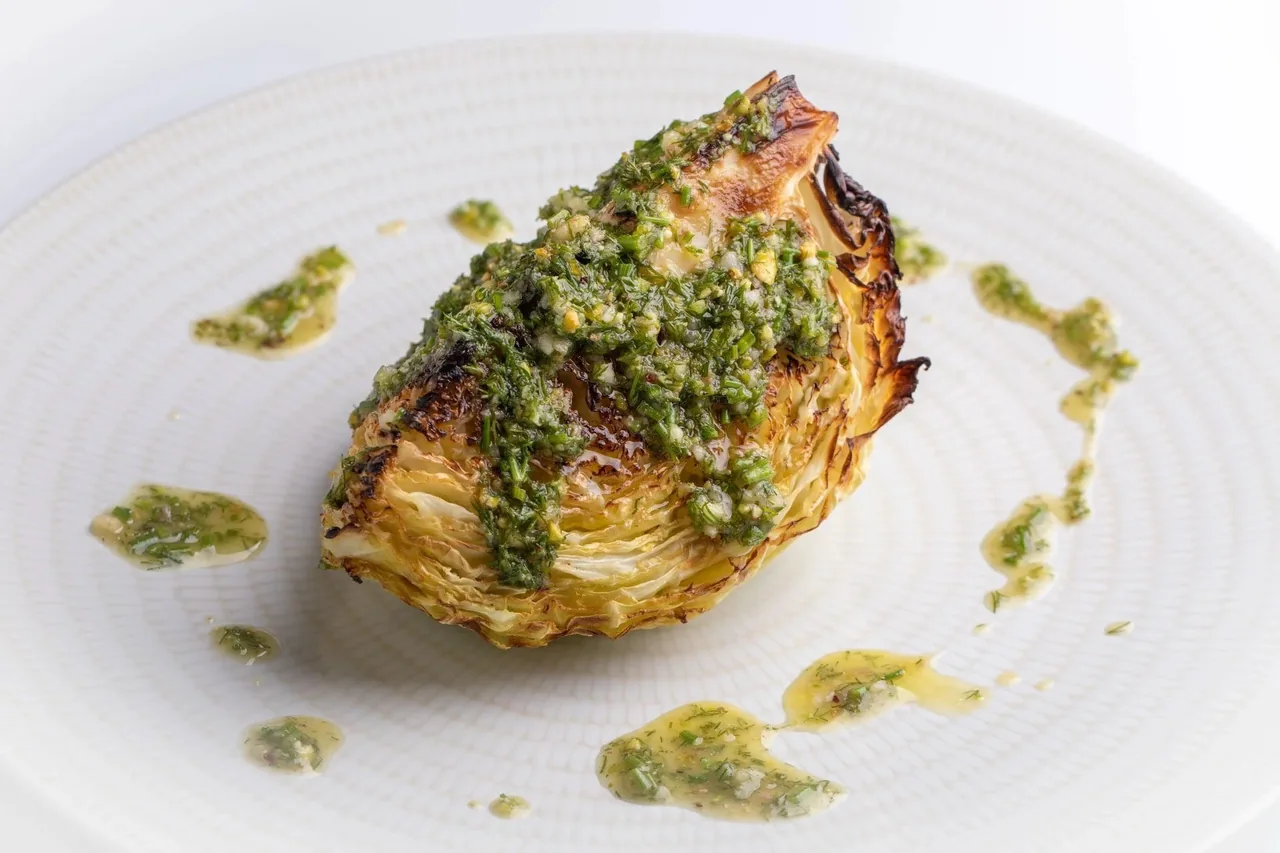 A grilled half cabbage with green sauce on a white plate