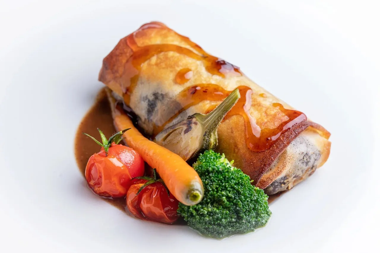 A golden baked parcel with roasted tomatoes, carrot and broccoli on a white plate