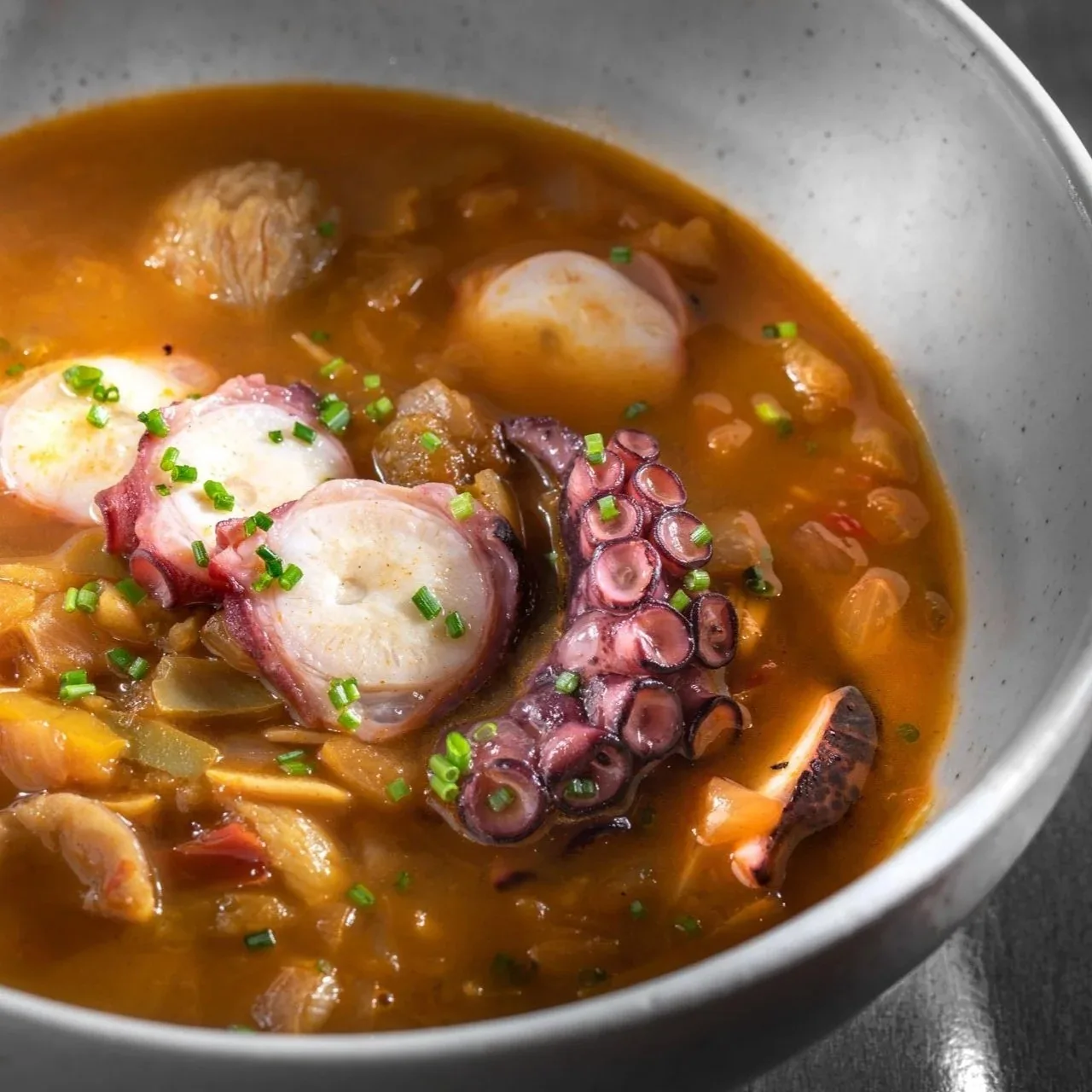 A grey bowl of orange stew with pieces of tentacle and other seafood