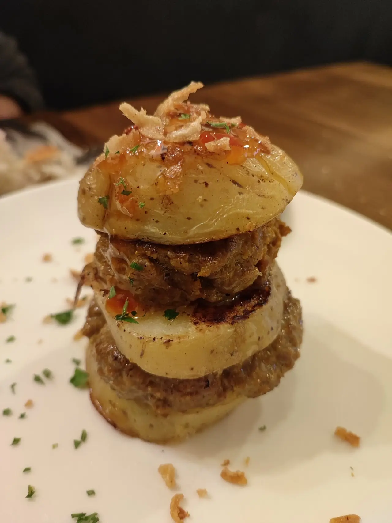 A stacked tower of layered potato slices and meat topped with crispy onions