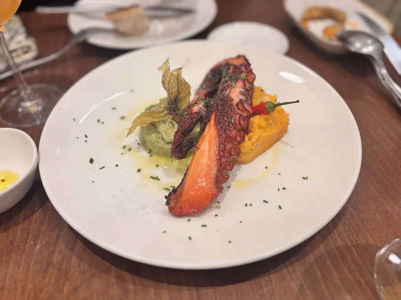 Grilled octopus tentacle over pumpkin and greens on a white plate